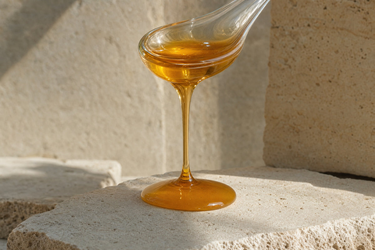 Thick amber liquid pouring slowly from a glass spoon onto a stone slab